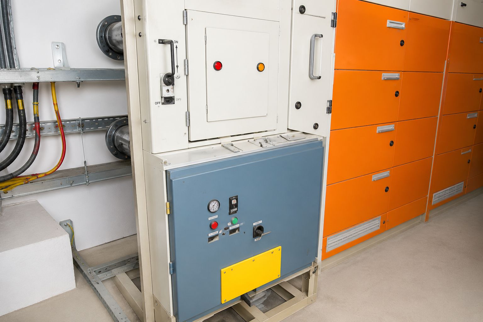 Switchroom containing cream and orange panel cubicles beside a wall of cable tray carrying glanded supply cables
