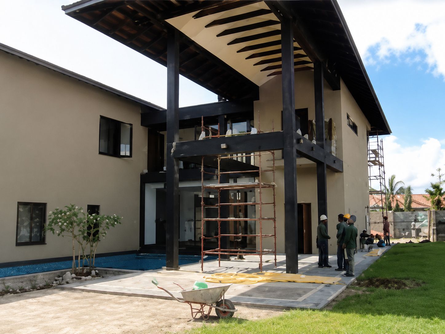 Two-storey residence under construction with exposed steel structure, scaffolding, coiled cable on the terrace and the site team working outside