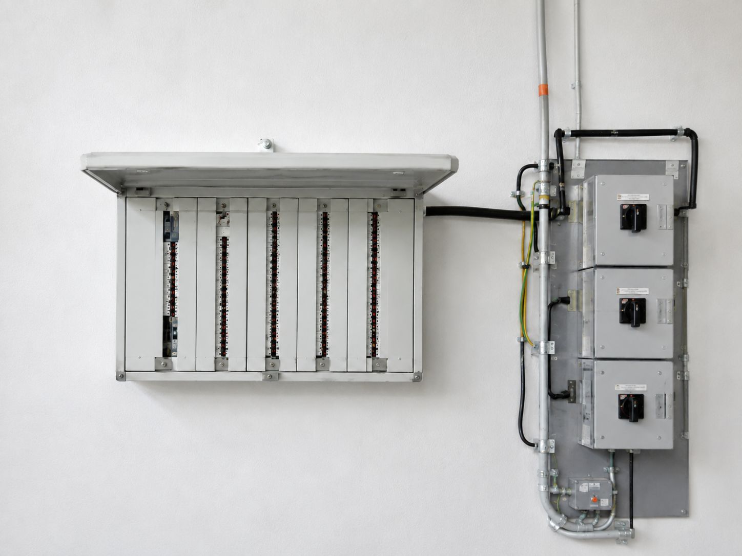 Wall-mounted distribution board with the door open showing rows of circuit breakers, beside three isolator enclosures on a backboard